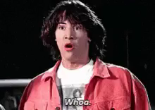 A young Keanu Reeves with scruffy black hair, white t-shirt and red jacket goes "whoa". 