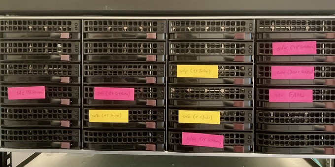Front panel of a 4U Supermicro server with 24 hard drive bays. Half of them have colorful stickies on them indicating those with bad sectors (pink) or those that are pretty new (yellow)