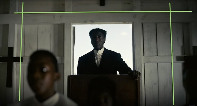 Screen grab of the movie Sinners by Ryan Coogler. A black pastor is standing inside a room made of white wooden planks and beams. He's forming a silhouette in front of an over-exposed white window. A cross is hanging on the wall screen left and a church boy is out of focus in the foreground. Green lines have been overlaid onto the image to  underscore that straight lines at the edges of the frame are actually pretty straight.